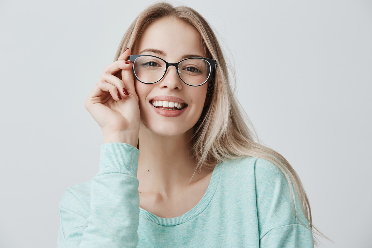девушка блондинка улыбается в очках придерживая рукой оправу