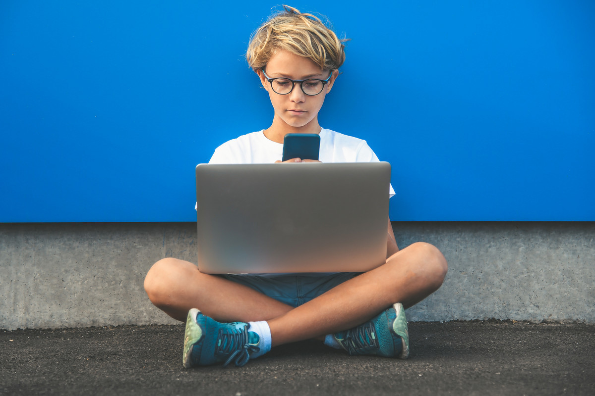 мальчик сидит в очках на фоне синей стены с ноутбуков и смотрит на монитор