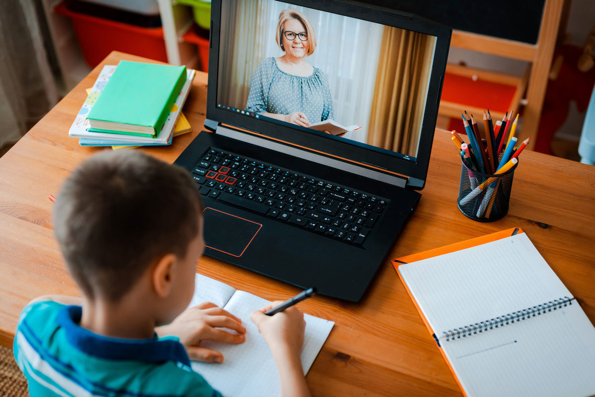 школьник учится за столом и находится на виртуальном уроке в ноутбуке видно его учителя