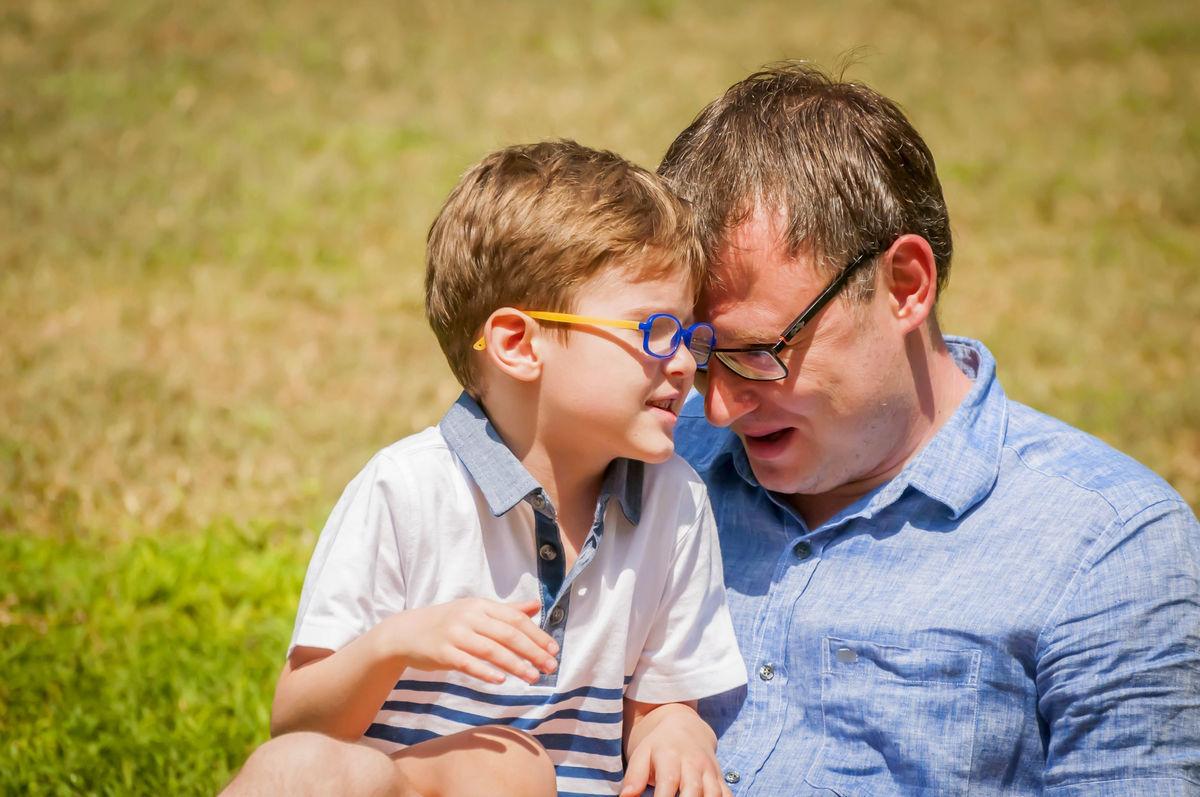 отец в очках и мальчиком ребенком играет на траве смеются